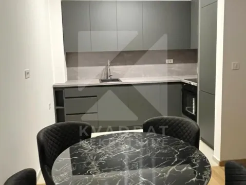 Moderna kuhinja sa tamnim elementima i trpezarijskim stolom u prvom planu. - image 3