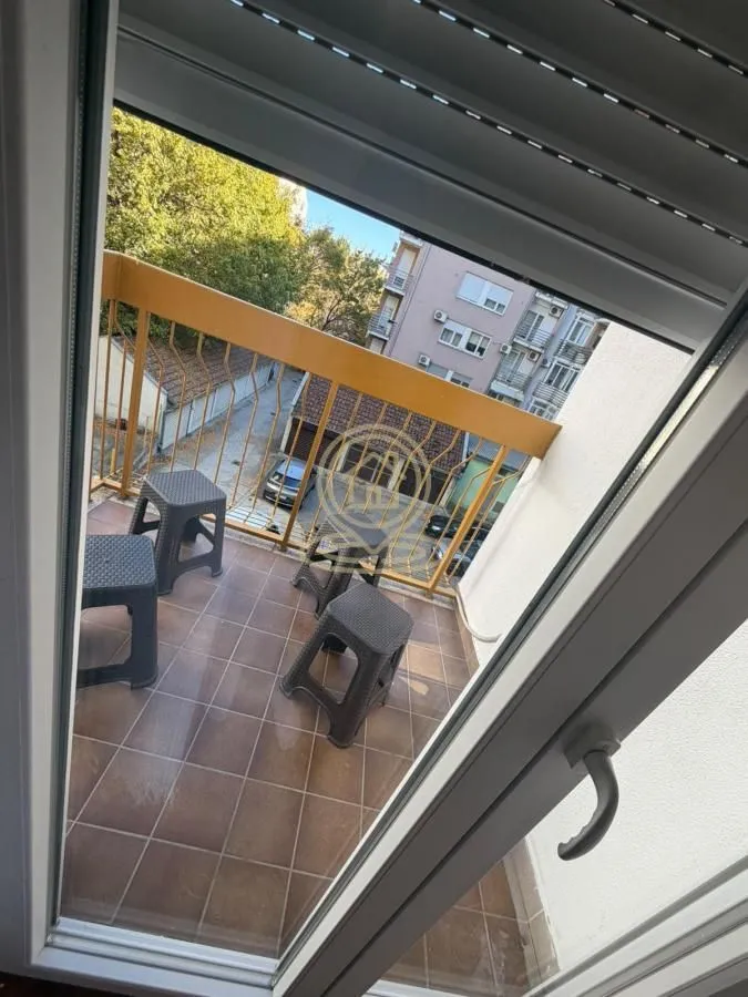 Pogled na popločanu terasu sa garniturom za sedenje kroz otvorena balkonska vrata.