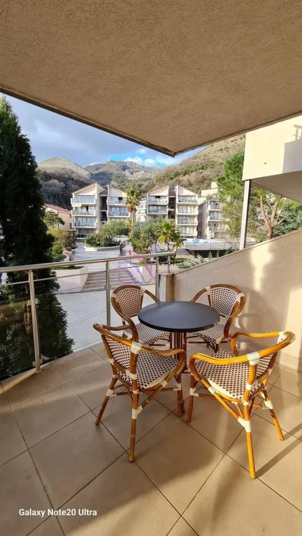 Namješten balkon sa stolom i četiri stolice, sa pogledom na dvorište zgrade i planine.