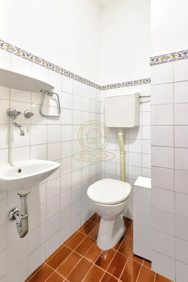 Small bathroom with white tiles, washbasin and toilet.