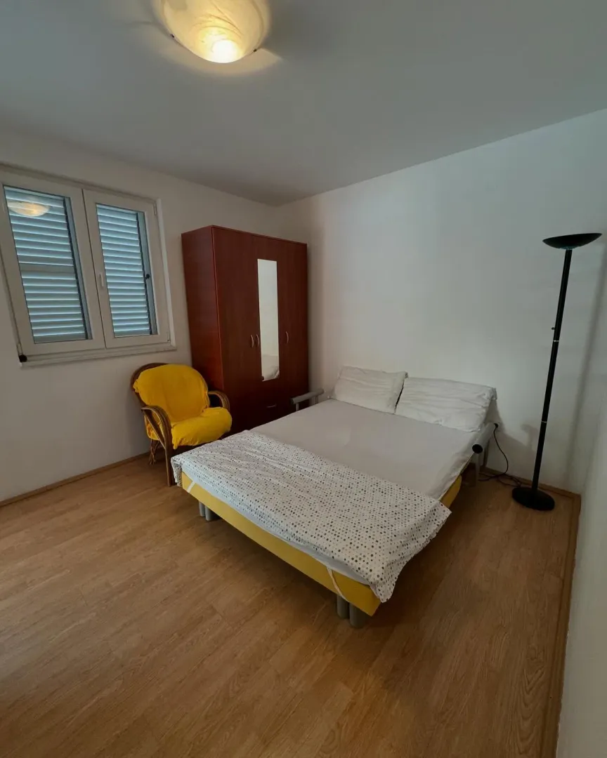 Spavaća soba sa bračnim krevetom, ormarom i drvenim podom.