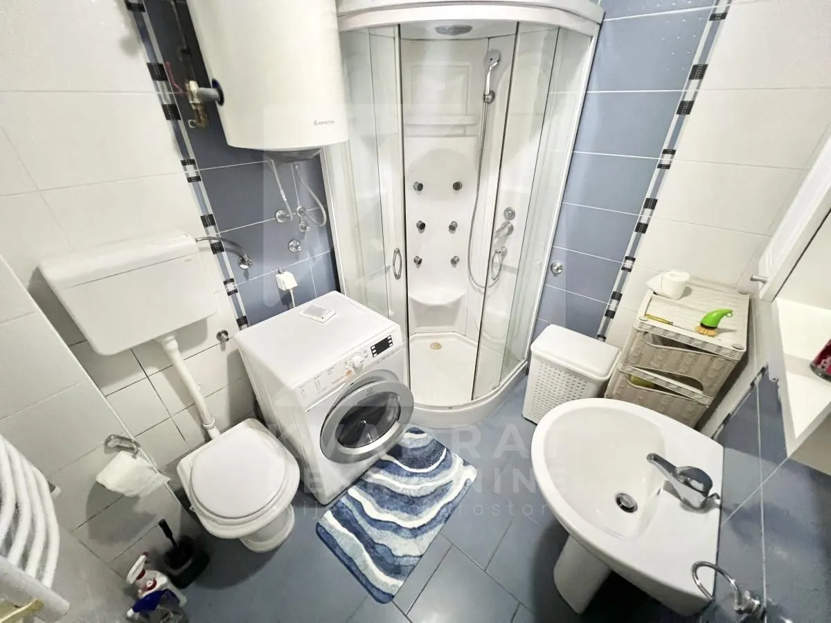 Manje kupatilo sa tuš kabinom, veš mašinom i sanitarijama.