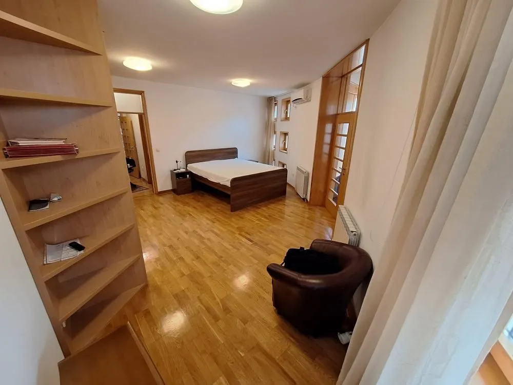 Spavaća soba sa bračnim krevetom, drvenim podom i policama.