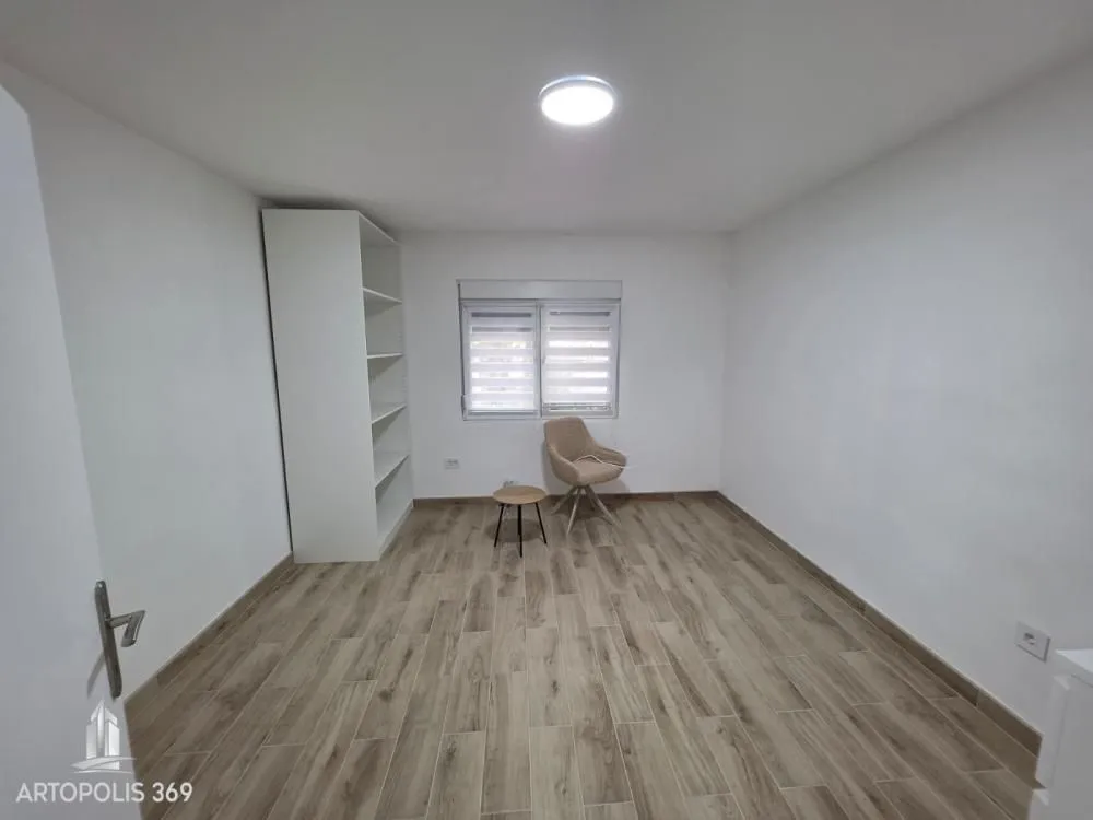 An empty room with white walls, wooden flooring, a wardrobe, and an armchair.