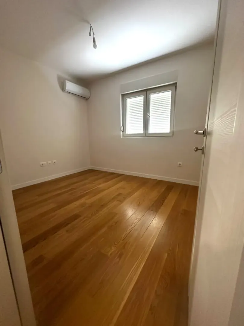 Empty room with wooden flooring, air conditioning unit, and a window.