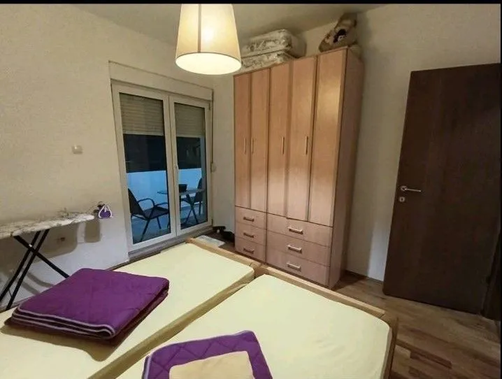 Jednostavna spavaća soba sa dva kreveta, ormarom i izlazom na terasu.