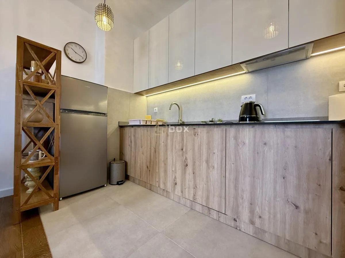 Small kitchen with wooden lower cabinets, a refrigerator, and white upper cabinets.