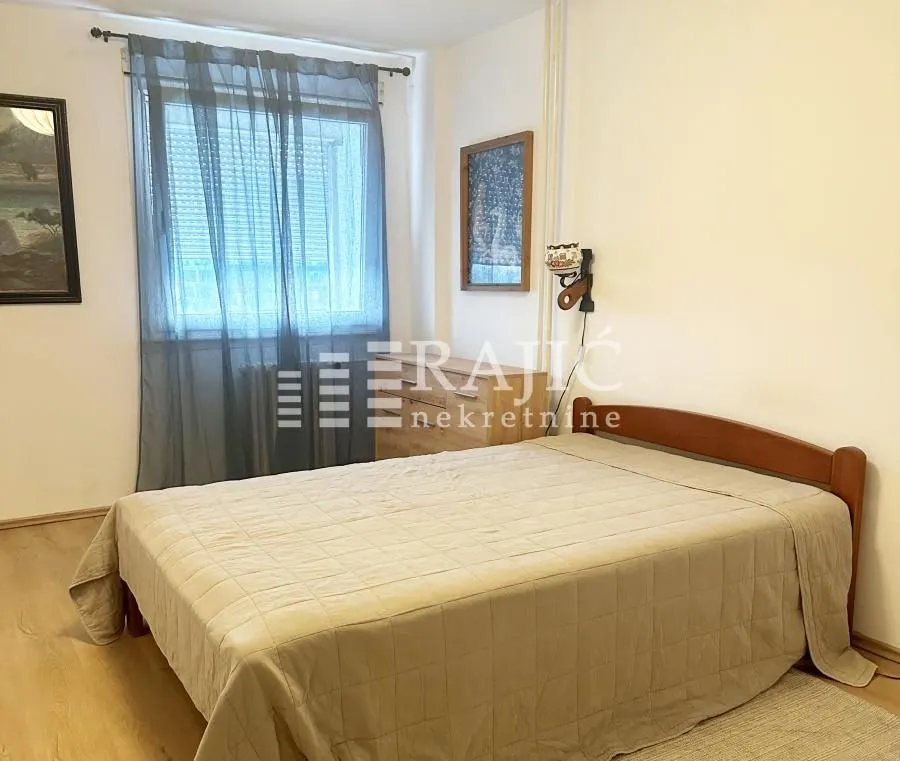 Furnished bedroom with a double bed and a window with curtains.