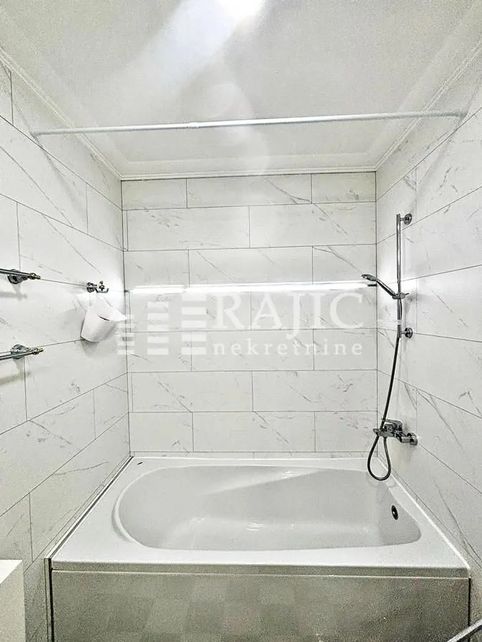 Smaller bathroom with a bathtub lined with marble tiles.
