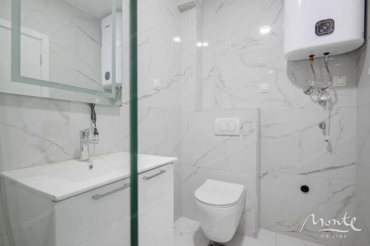 Manje kupatilo sa bijelim pločicama, umivaonikom i wc šoljom.