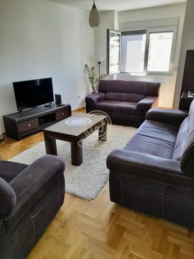 Dnevna soba sa garniturom, televizorom i drvenim podom.