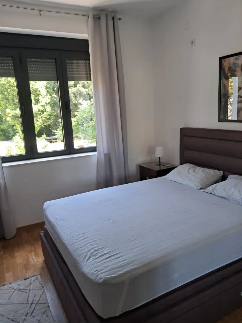 Furnished bedroom with a double bed and a window overlooking greenery.