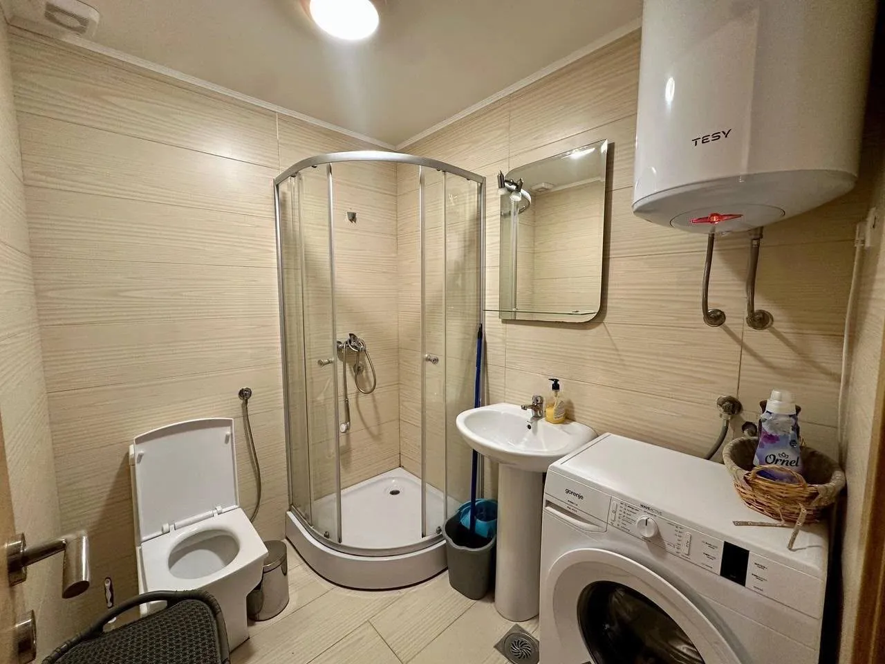 Small bathroom with a shower cabin, sink, toilet, and washing machine.