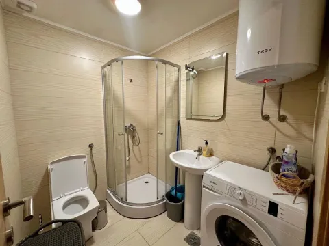 Small bathroom with a shower cabin, sink, toilet, and washing machine. - image 3