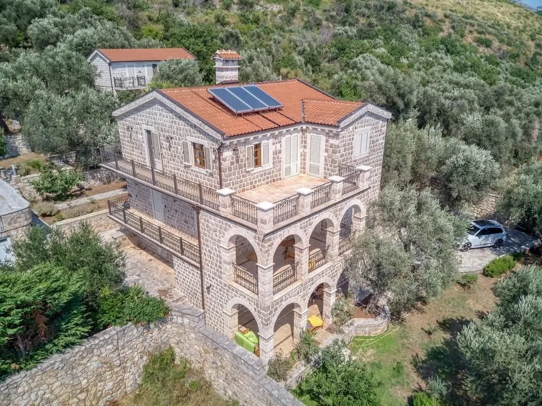 Pogled iz vazduha na kamenu kuću sa terasama i dvorištem okruženom zelenilom.
