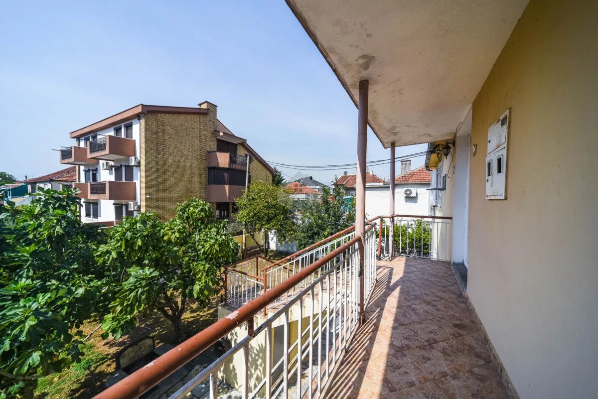 Natkriveni balkon sa pogledom na okolne zgrade i zeleni yard.