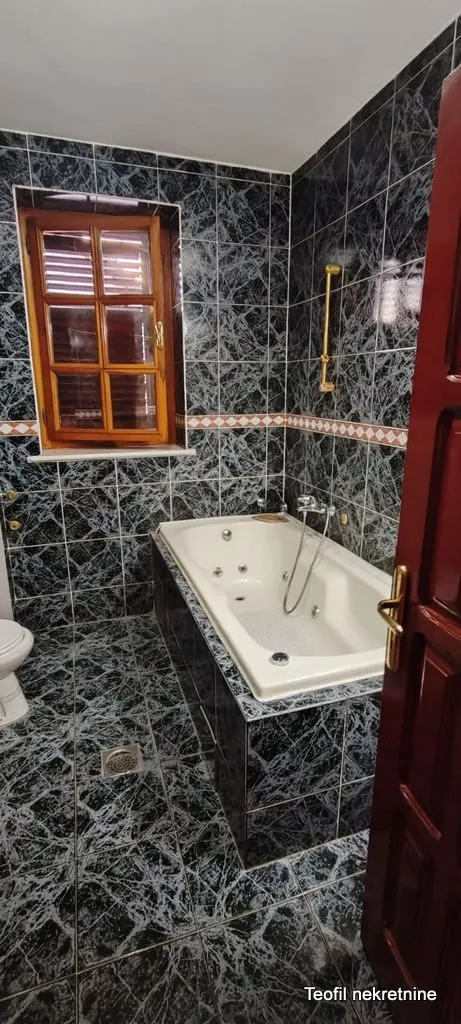 Bathroom tiled in dark marble with a bathtub and a window.