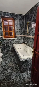 Bathroom tiled in dark marble with a bathtub and a window. - image 16