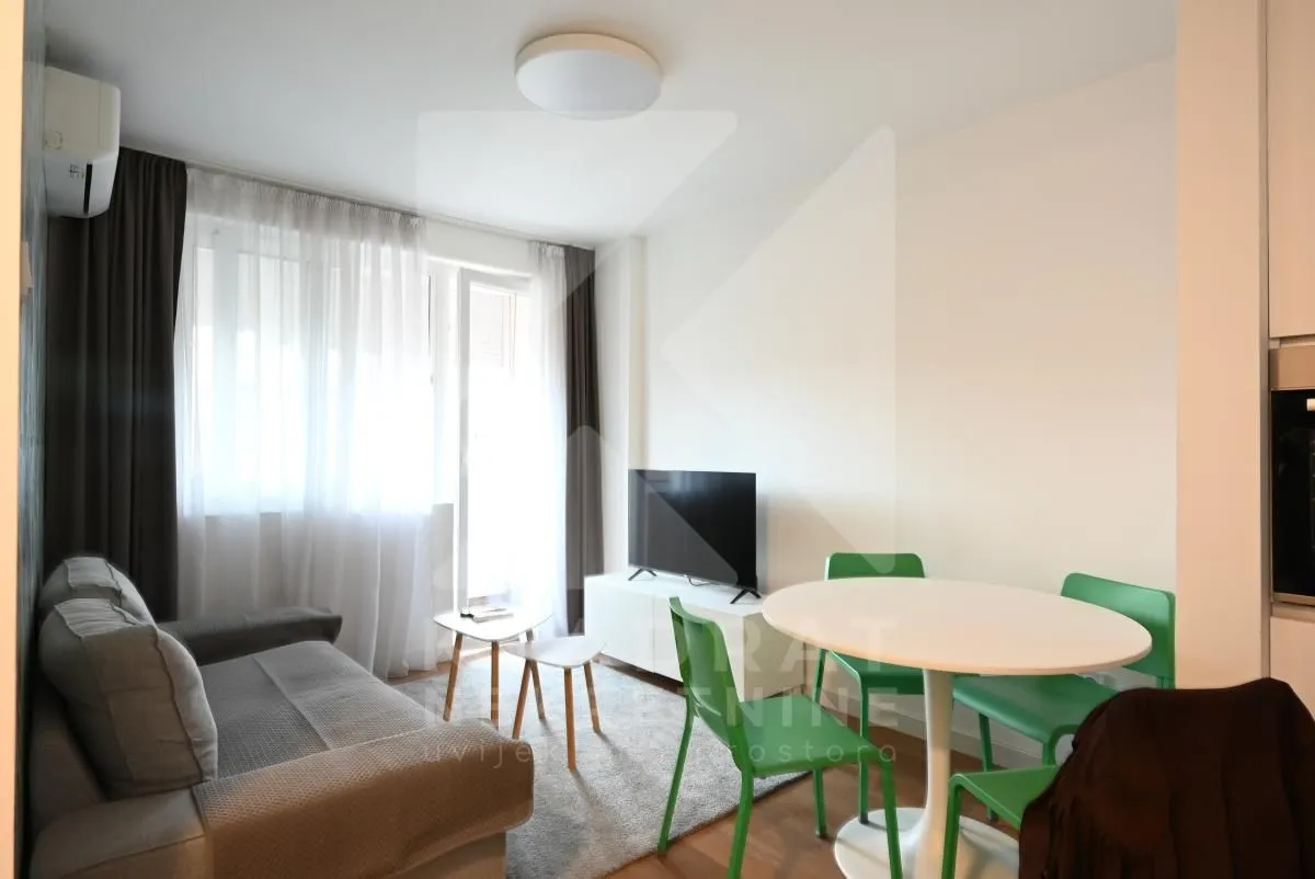 Living room with a sofa, TV, and a dining table with green chairs.