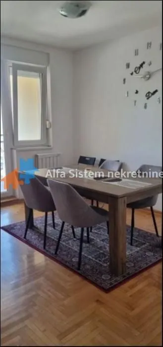 Trpezarija sa drvenim stolom i tapaciranim stolicama.