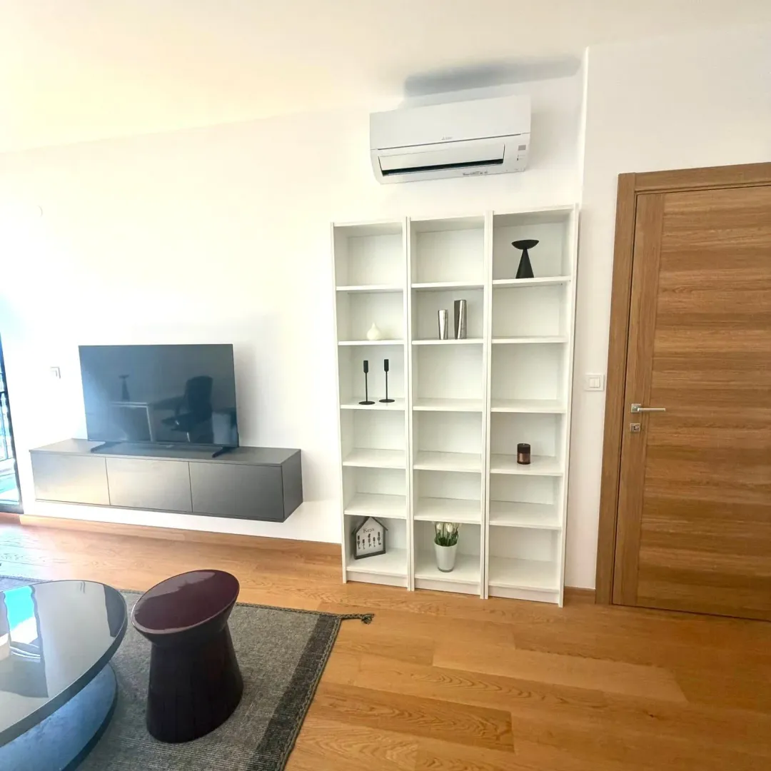 Modern living room with a TV unit, white shelving unit, and air conditioning.