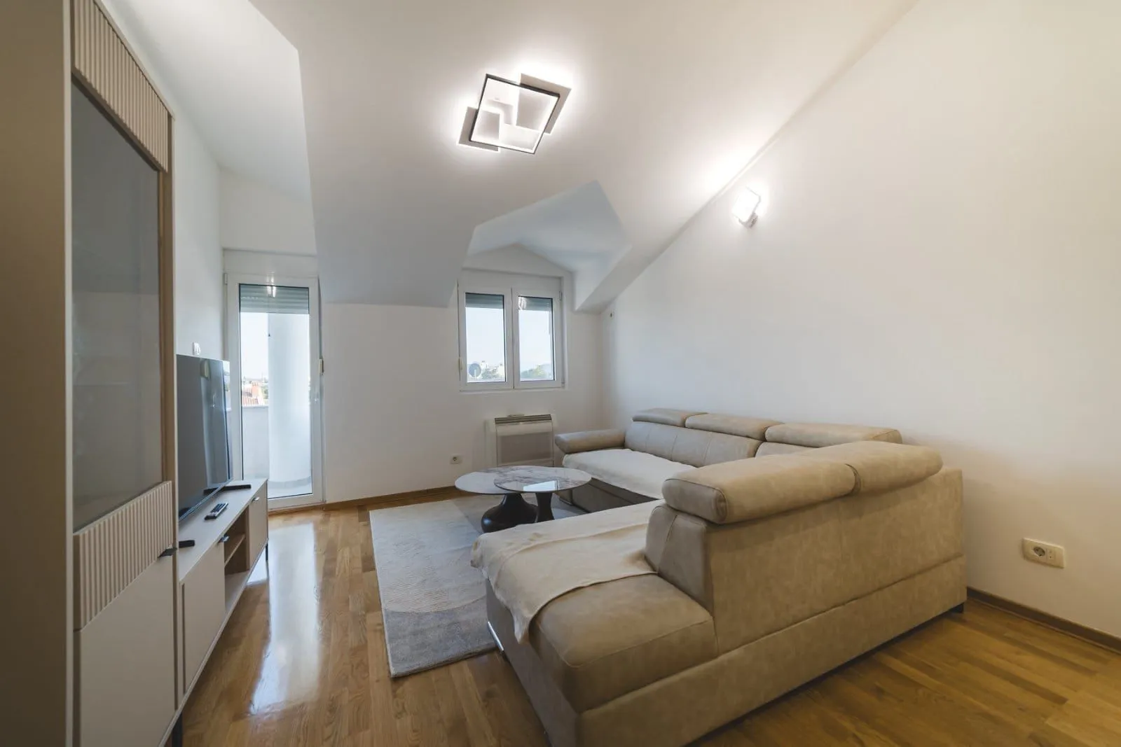 Bright living room with a sofa set, TV unit, and access to the terrace.