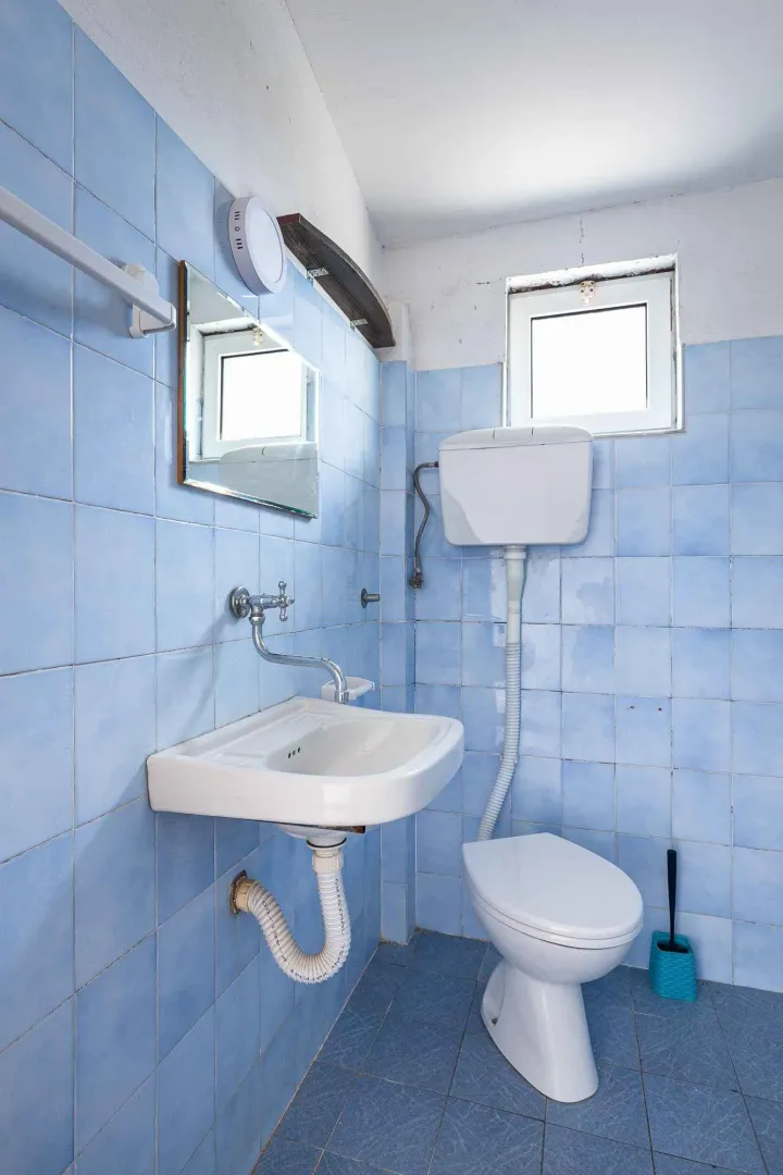 Manje kupatilo obloženo plavim pločicama sa umivaonikom i WC šoljom.