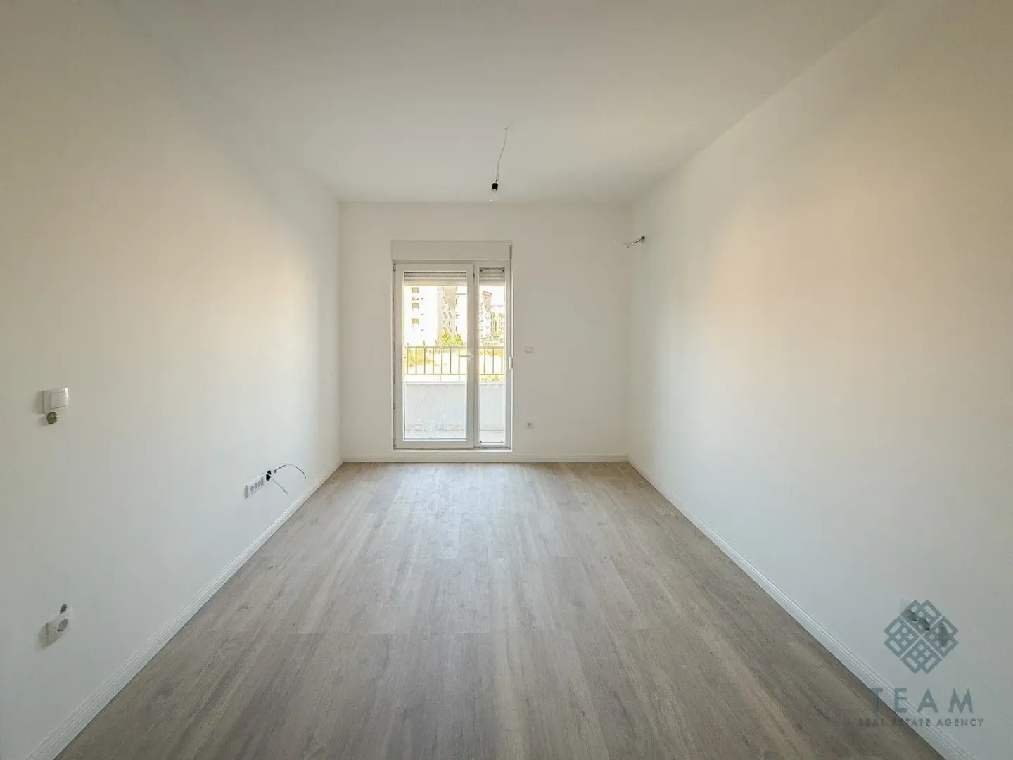 Prazna neopremljena soba sa bijelim zidovima i drvenim podom, sa izlazom na terasu.