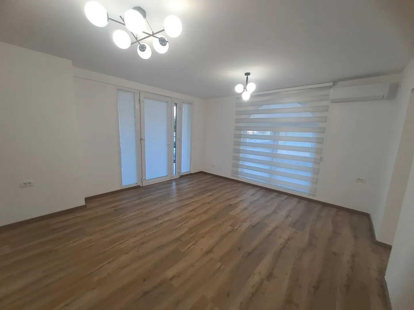 Empty room with wooden flooring, white walls, and modern ceiling lighting.