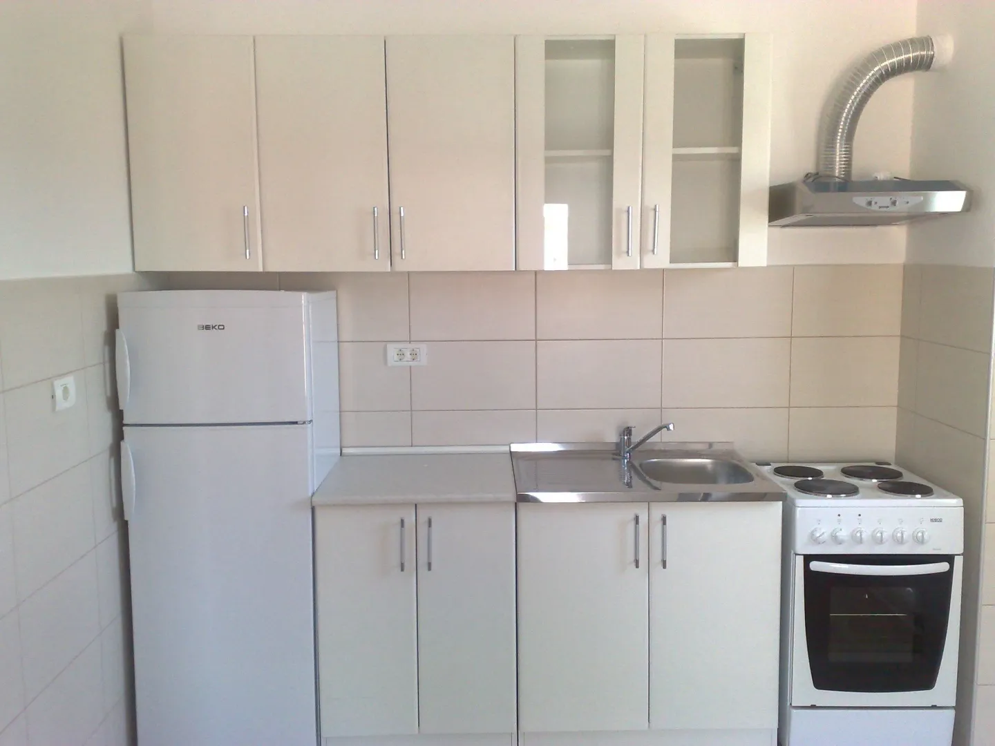 Jednostavna bijela kuhinja sa frižiderom, šporetom i sudoperom.