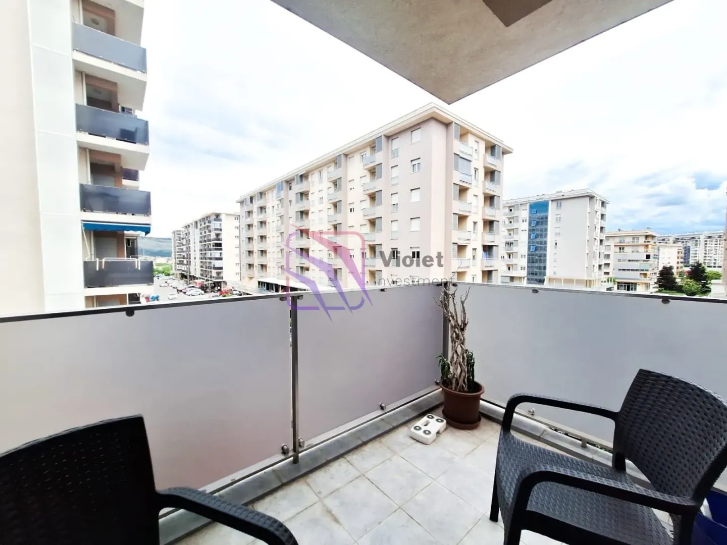 Natkriveni balkon sa garniturom za sjedenje i pogledom na okolne zgrade.
