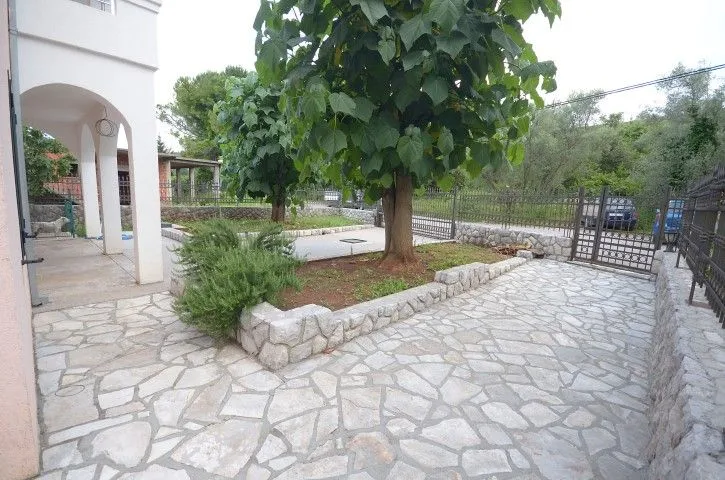 Popločano dvorište sa drvećem i zelenilom ispred kuće.
