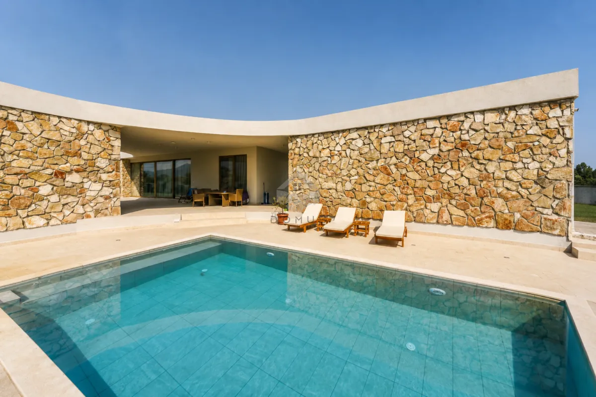 Yard with a swimming pool and sun loungers in front of a modern stone-clad villa.