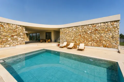 Yard with a swimming pool and sun loungers in front of a modern stone-clad villa. - image 36