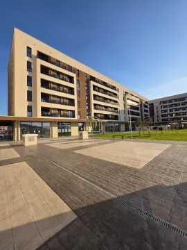Pogled na spoljašnjost moderne stambene zgrade sa popločanim dvorištem i uređenom travnatom površinom. - image 11