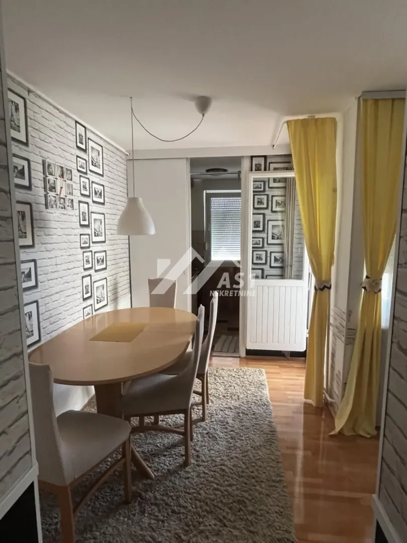 Trpezarija sa drvenim stolom i stolicama, ukrašena zidom od cigle i brojnim ramovima za slike.