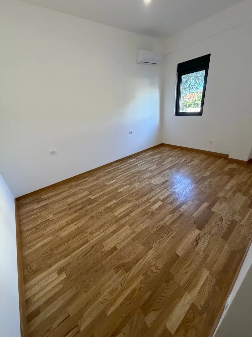 Prazna soba sa drvenim podom i bijelim zidovima.