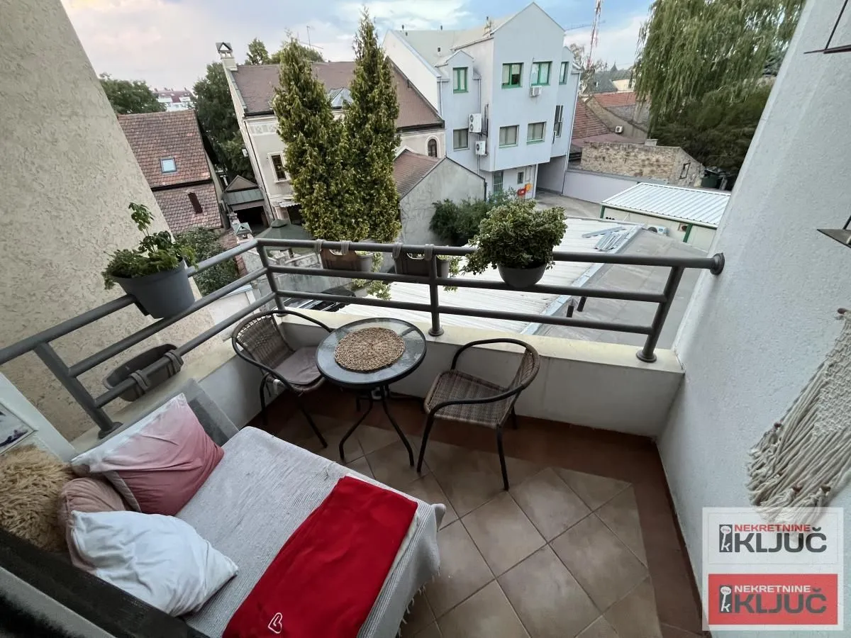 Namešten balkon sa garniturom za sedenje i pogledom na okolne zgrade.