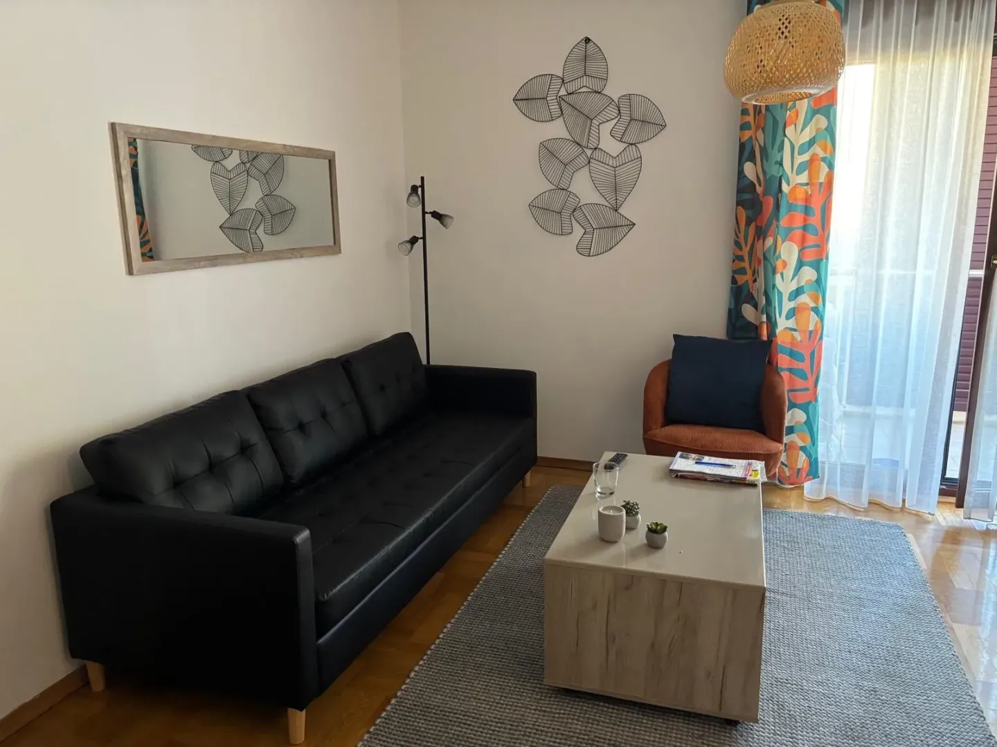 Svijetla dnevna soba sa crnom kožnom garniturom, klub stolom i dekorativnim detaljima na zidu.