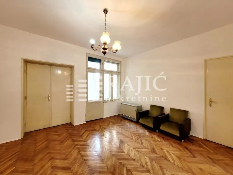 Empty living room with parquet flooring, a chandelier, and a couple of armchairs.