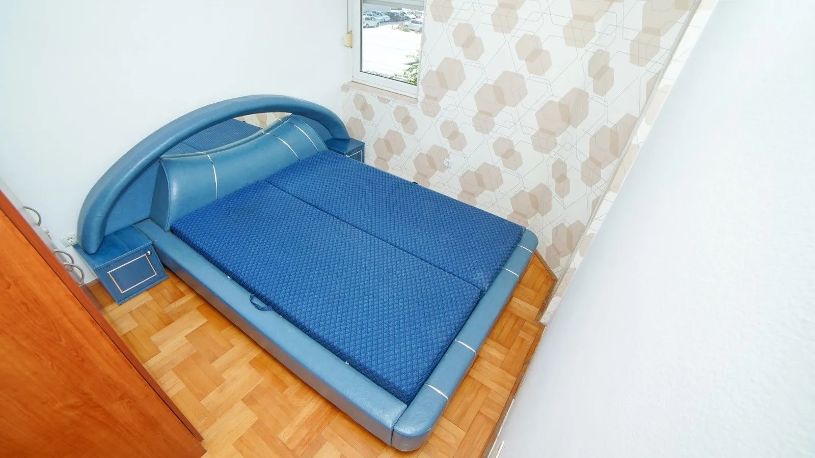 Bright bedroom with a large blue bed and parquet flooring.
