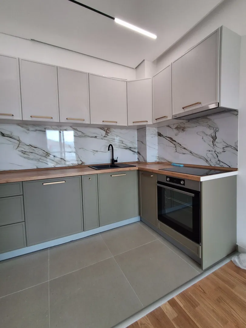 Modern corner kitchen with green base cabinets, white upper cabinets, and a marble-patterned backsplash.