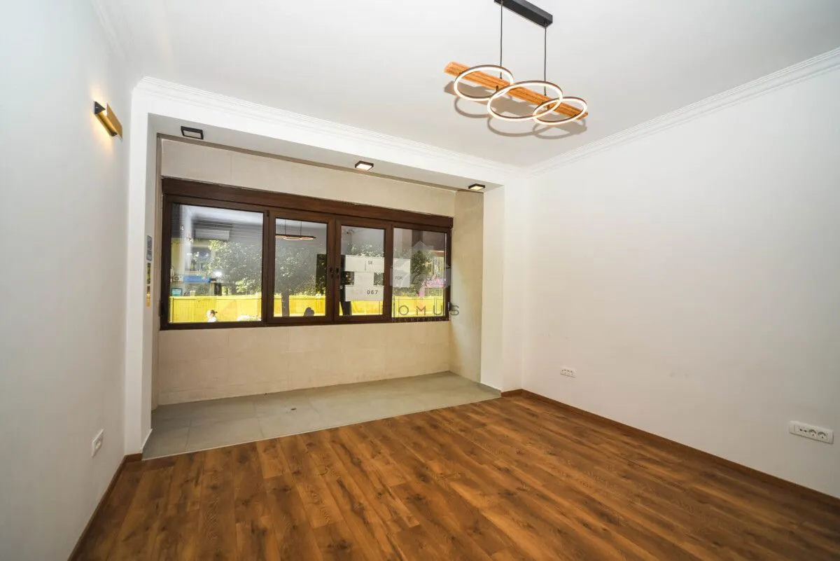 Empty room with wooden flooring, a large window, and a modern ceiling light fixture.