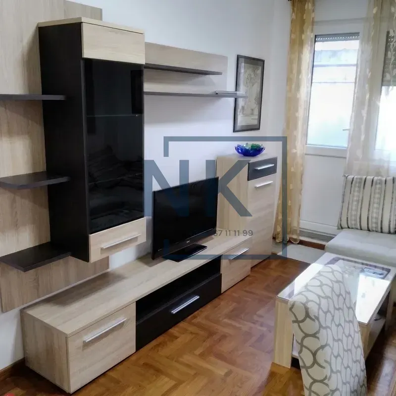 Dnevna soba sa TV elementom, garniturom i parketom na podu.