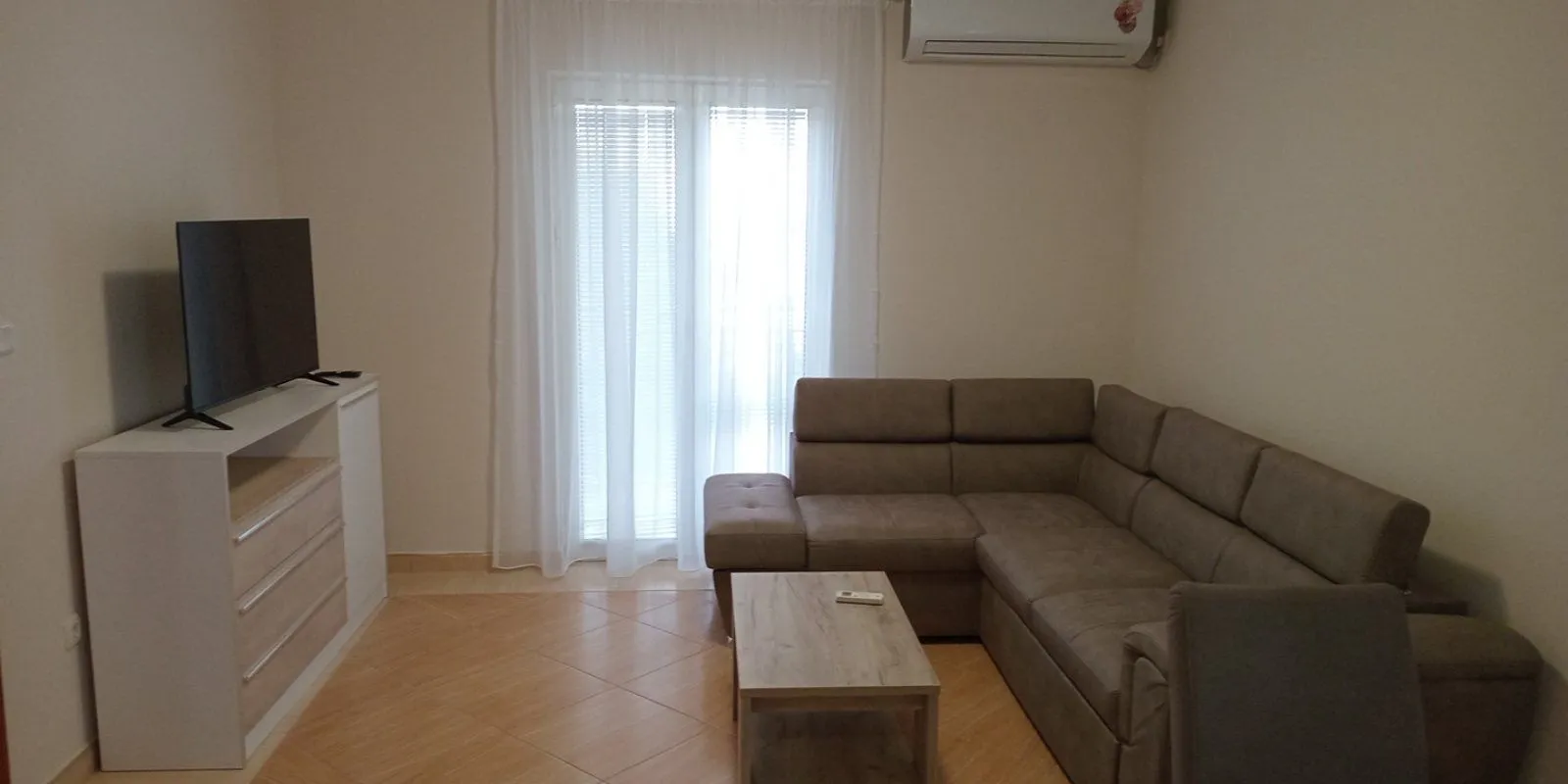 Living room with a corner sofa, TV unit and air conditioning.