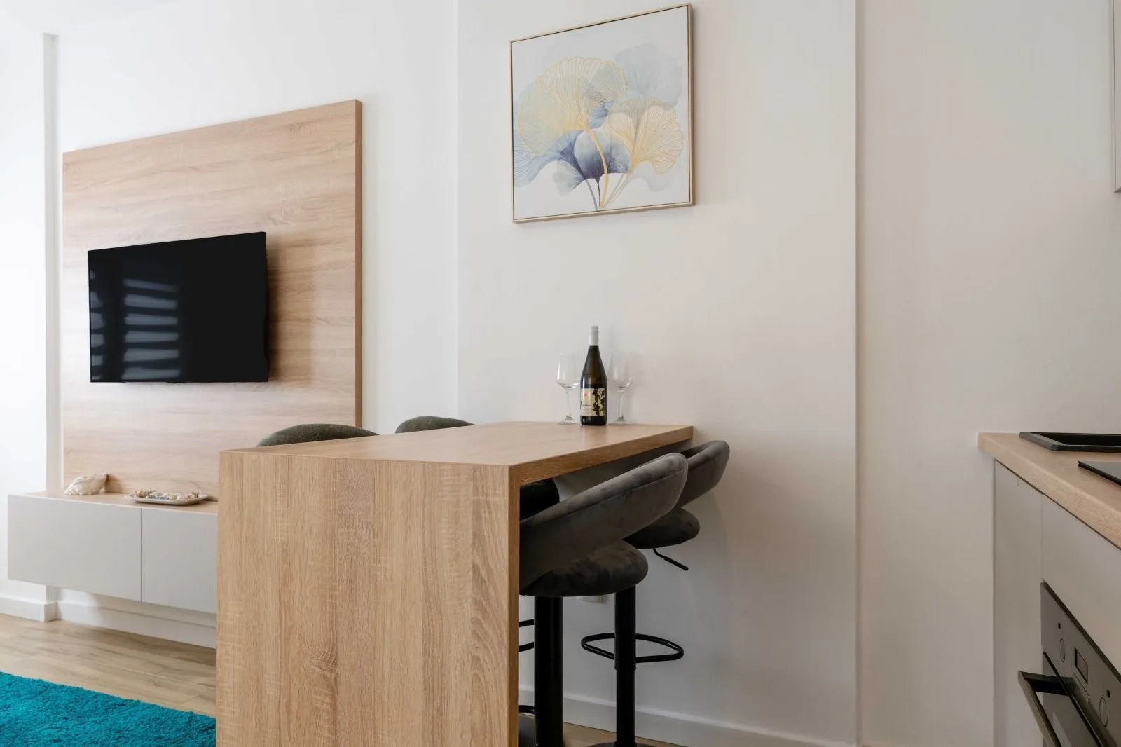Living room with a dining table, bar stools, and a wall-mounted TV.