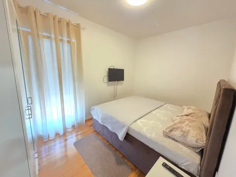 Manja spavaća soba sa bračnim krevetom, prozorom i televizorom na zidu. - image 3