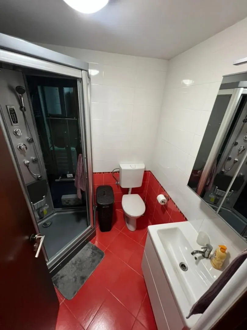 Kupatilo opremljeno tuš kabinom, umivaonikom i wc šoljom sa crvenim keramičkim pločicama.