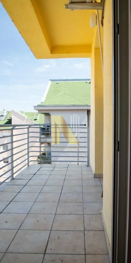 Natkriveni balkon sa popločanim podom i metalnom ogradom.
