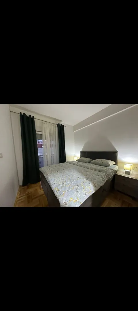 Furnished bedroom with a double bed, nightstands, and a window with dark curtains.